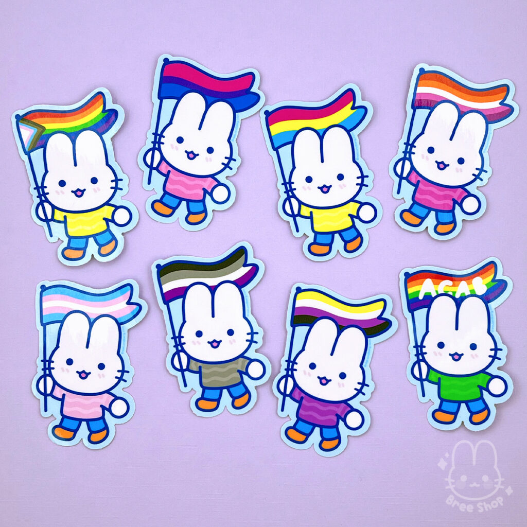 Photo of eight stickers, each is the same cute stylized white bunny character wearing a colorful sweater and smiling while holding up different pride flags.