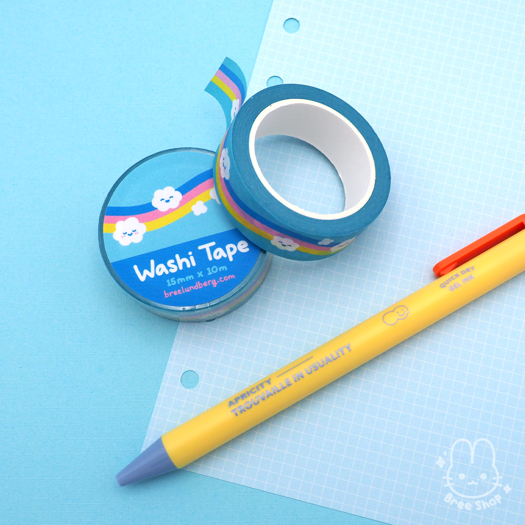 Photo of light blue washi tape rolls with cute illustrated clouds with happy faces patterned over a wavy rainbow in bright blue, pink, and yellow.